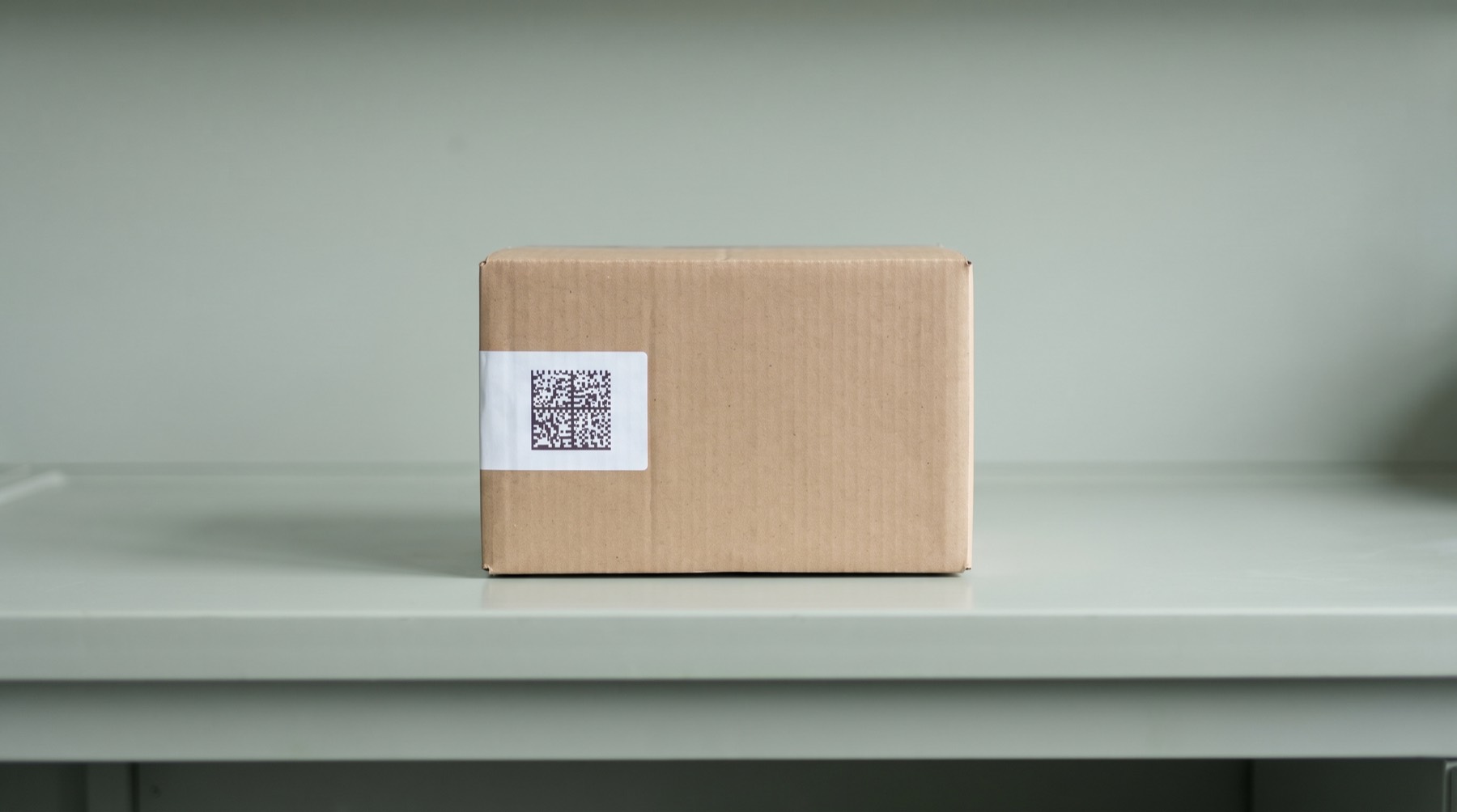 A plain box standing alone on an empty bench, with a small printed label carrying a machine-readable code